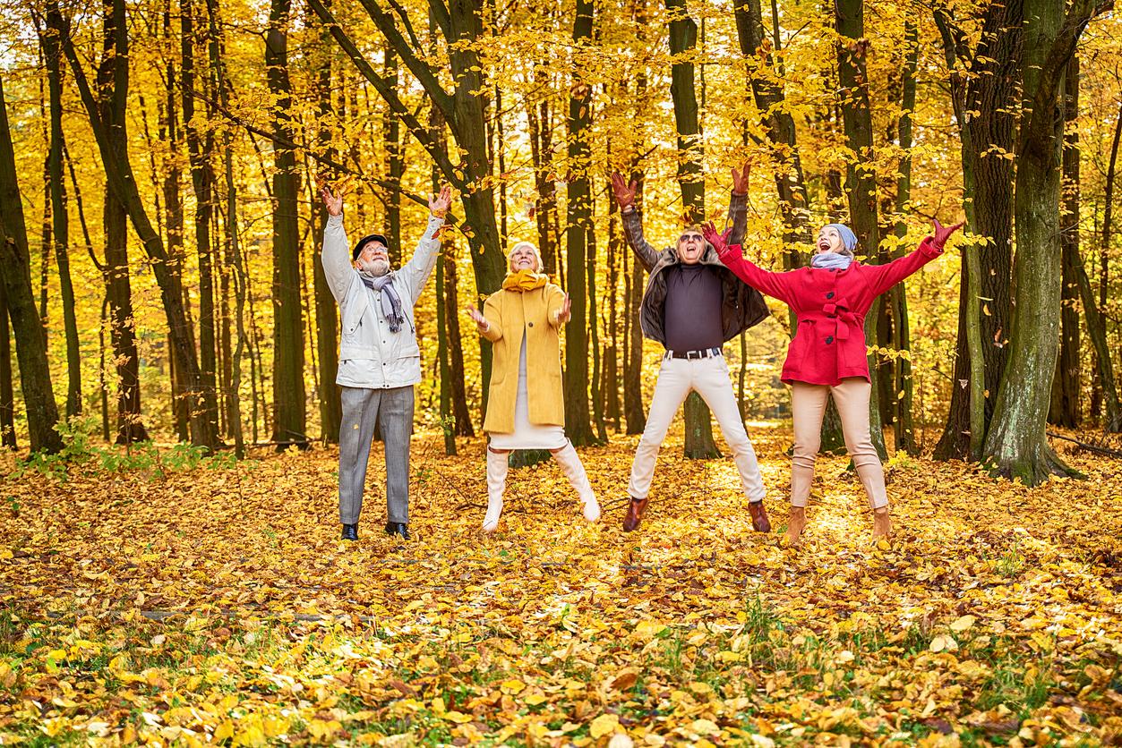 Group of happy seniors laughing and playing in golden fall leaves